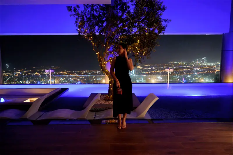 Amaya Lala beside a rooftop infinity pool at night, the city lit below