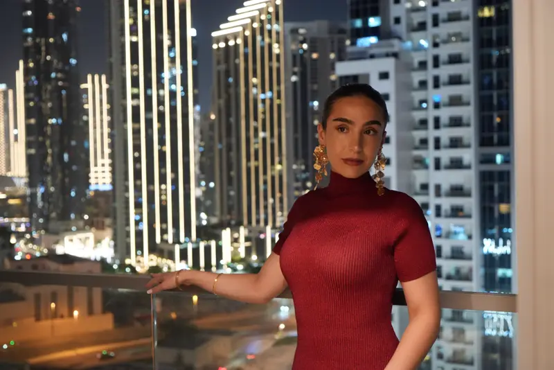 Amaya Lala in a red dress on a balcony against the lit Dubai skyline
