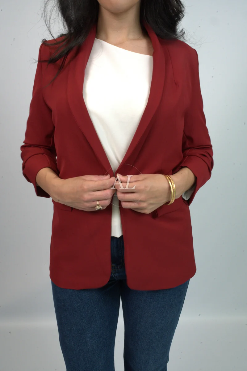 Amaya Lala fastening a deep-red tailored blazer worn open over a cream top with mid-blue jeans and a gold bangle, Kurt Muller campaign still